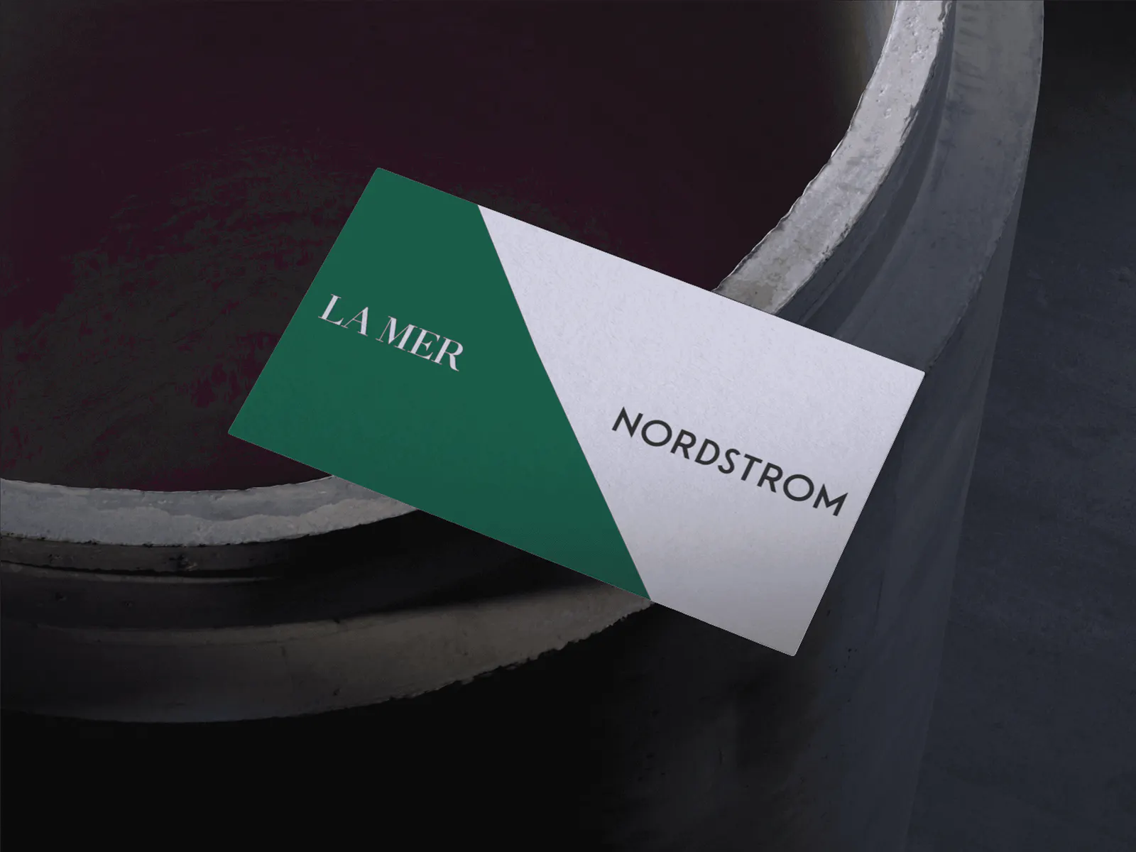 A business card resting on a concrete ledge, split diagonally into a green half reading La Mer and a white half reading Nordstrom